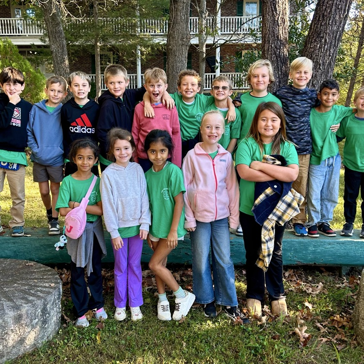 Group of young children in green shirts posing for a picture in a grassy area.