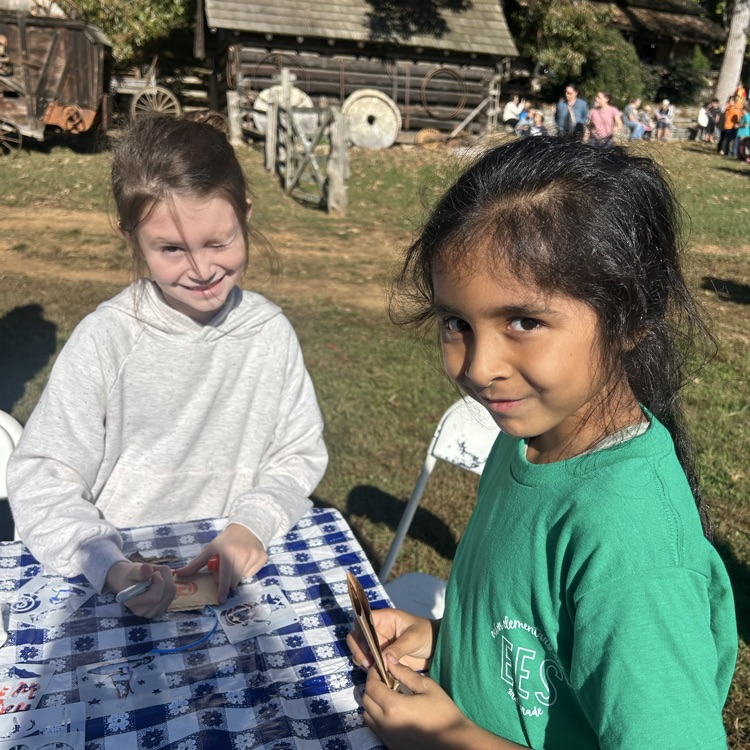 Two girls sit at a table with a blue and white tablecloth. One holds a small container.