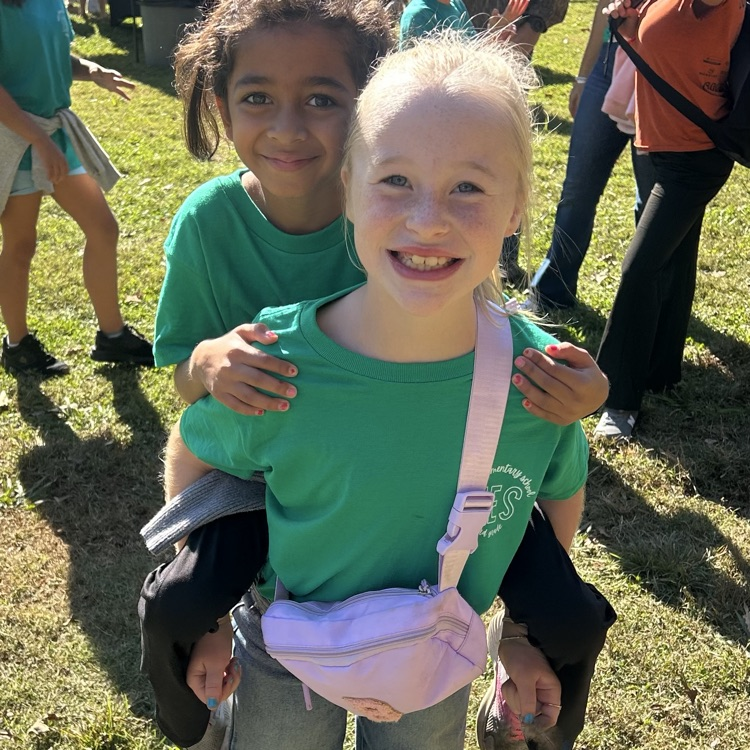 Two young girls in green shirts standing together, one smiling and the other looking into the camera.
