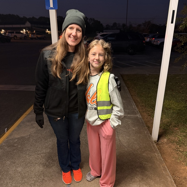 A woman and a young girl stand outside in a parking lot at night.