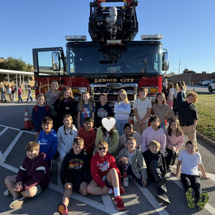 Group of children and adults posing with a fire truck in the background.