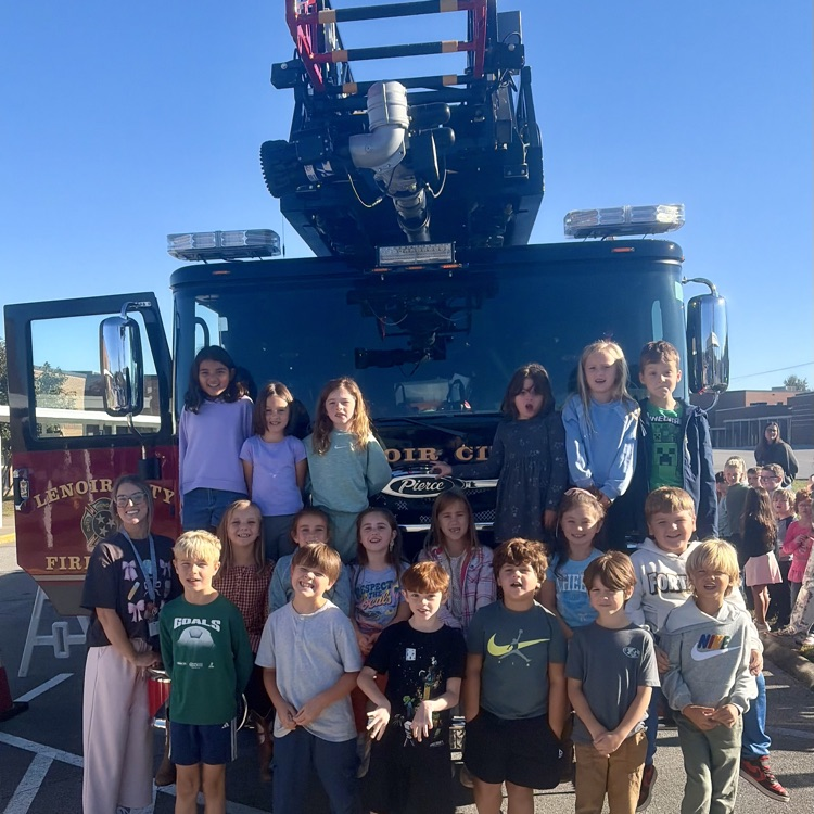 Students standing in front of a fire truck with the ladder raised, smiling and looking at the camera.