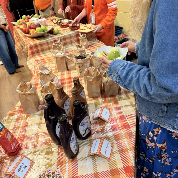 Table with food, including fruit and syrups, and people getting food in bags.
