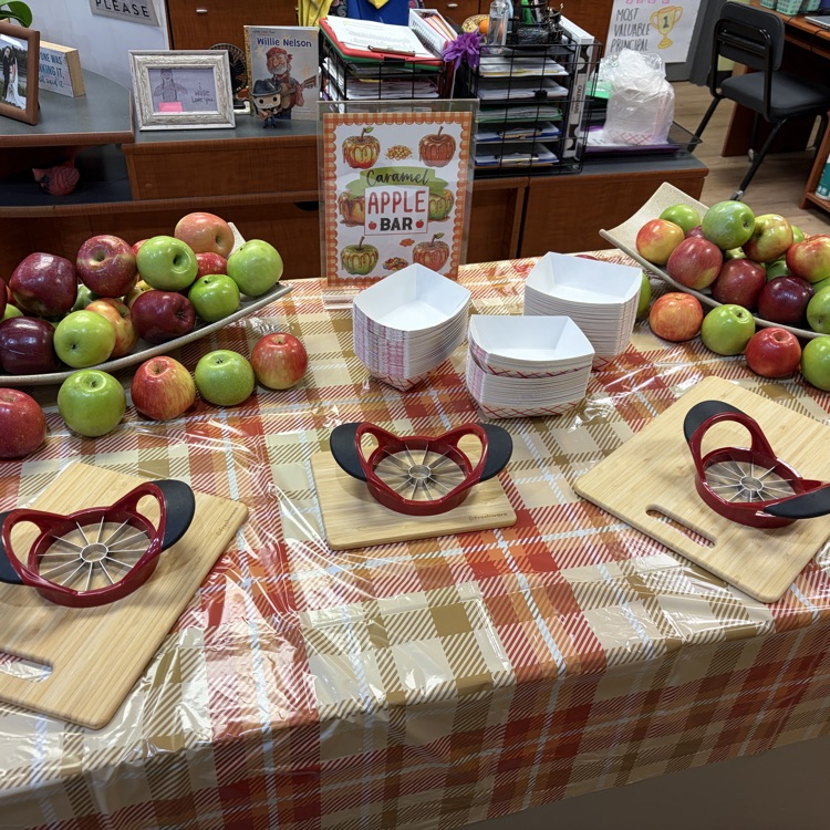 A table displays apples with apple slicers and cutting boards on a red and white checkered tablecloth.