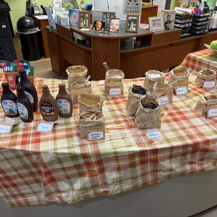 Table with a plaid tablecloth displaying various food items in brown paper bags with labels.