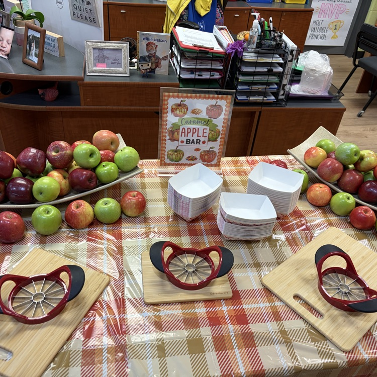 A table with apples, apple slicers, bowls, and a sign that says 'Apple'.
