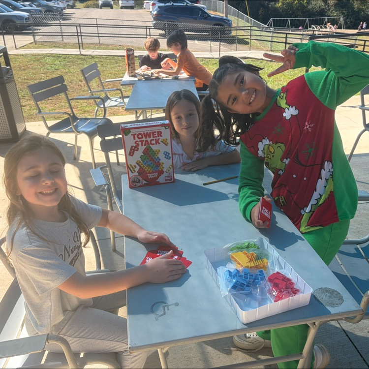 Three children seated at a table, two wearing sweatshirts, one holding a container with building blocks.