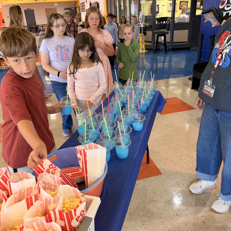 Children gather around a table with popcorn and blue drinks. The table is covered in a blue cloth.