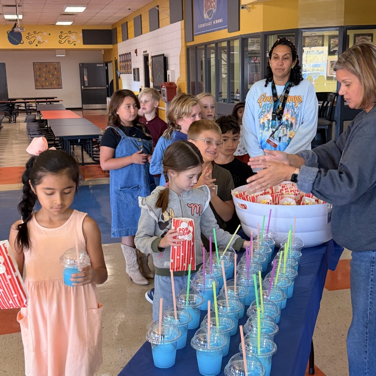 A group of children and adults gather around a table with cups, straws, and a large container.
