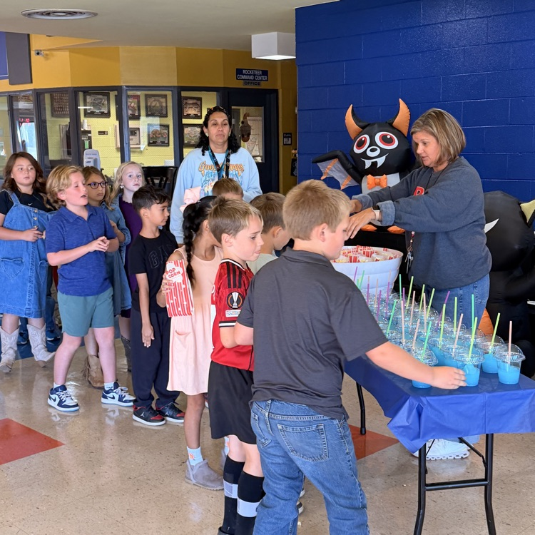 Kids line up to receive drinks from a table in a hallway. Some wear sneakers.