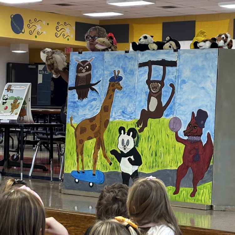 Classroom with a painted wall featuring animals. Children seated on the floor, watching the wall.