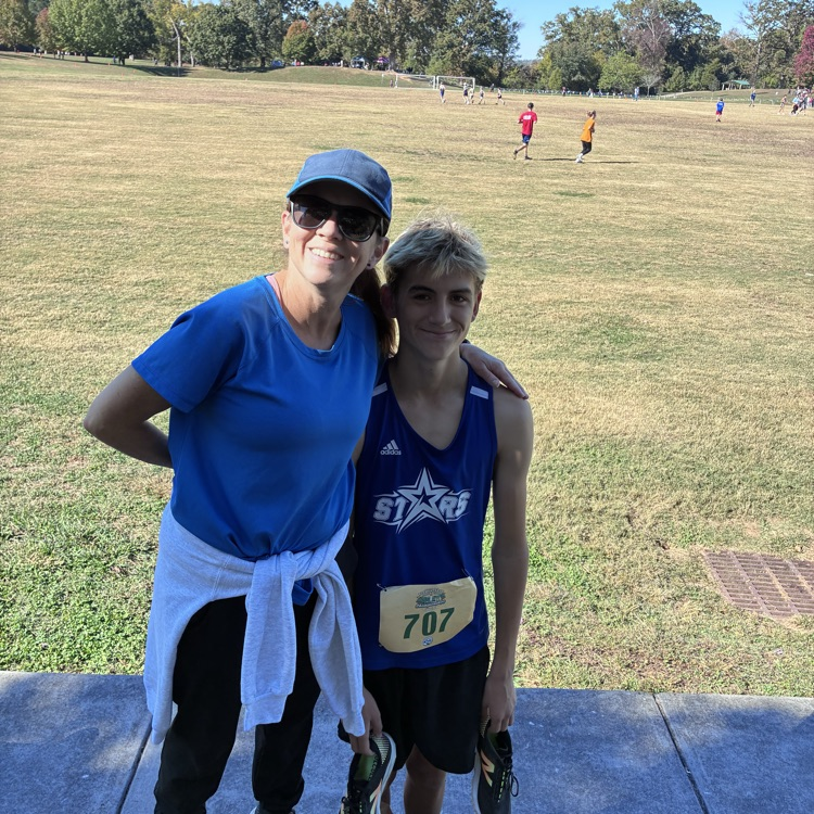 Two people standing on a path, one wearing a blue shirt and the other in a blue track uniform.