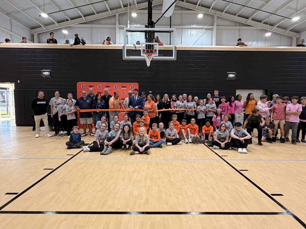 A group of people standing and sitting on a basketball court with orange ribbons tied to the railings.
