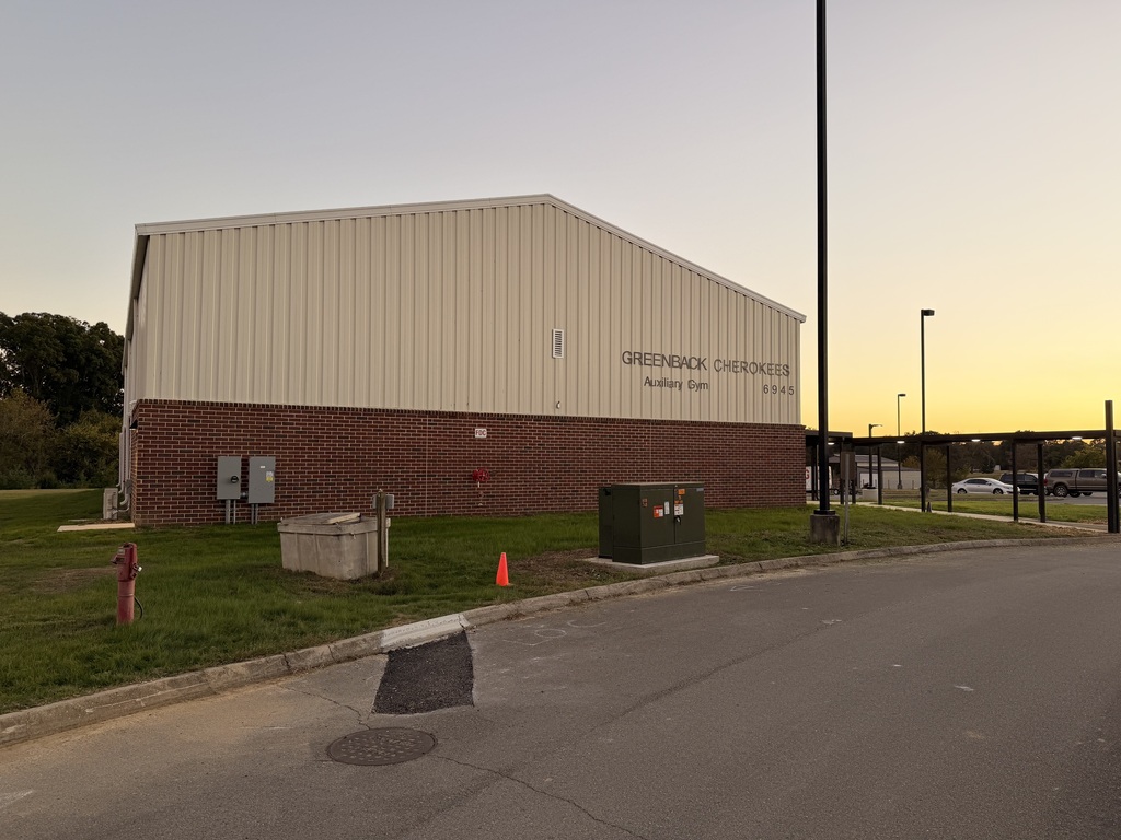 A building with a large sign. A road in front of the building. A fire hydrant, cone, and meter box near the road.