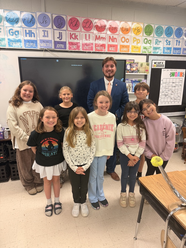 Students stand together in a classroom, with one boy in suit and tie behind them.