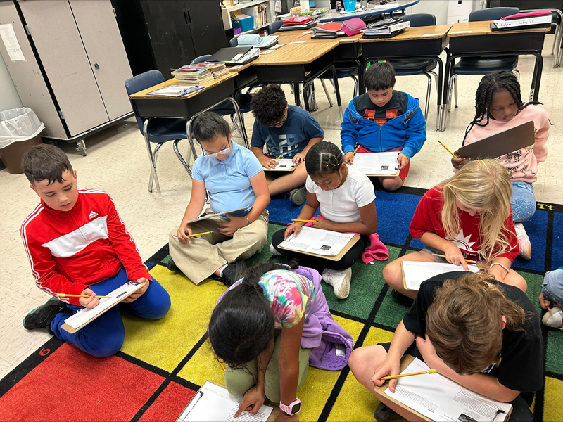 students seated on classroom carpet writing