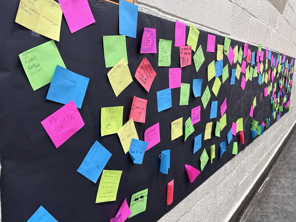 Photo of a black banner with sticky notes of gratitude hanging on the wall. 