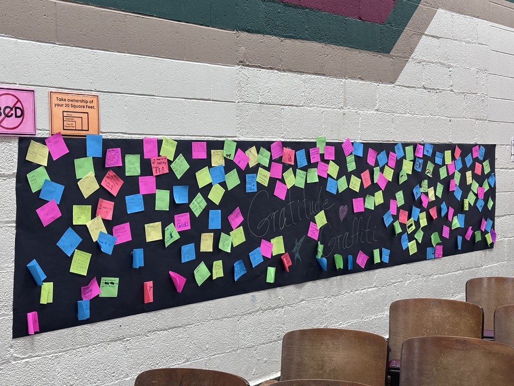 Photo of a black banner with sticky notes of gratitude hanging on the wall. 