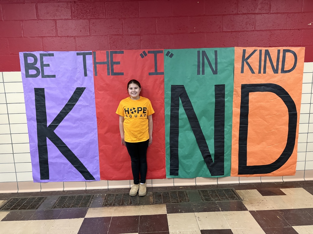 Student posed infront of a poster as the "i" in the word "Kind"