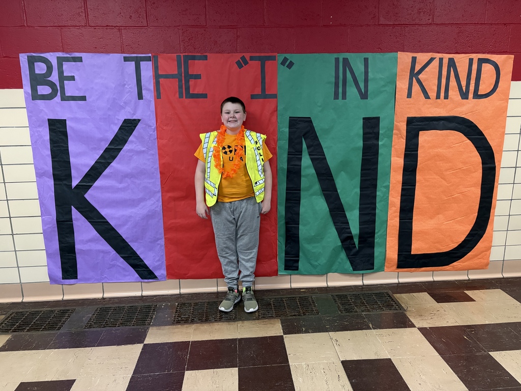 Student posed infront of a poster as the "i" in the word "Kind"