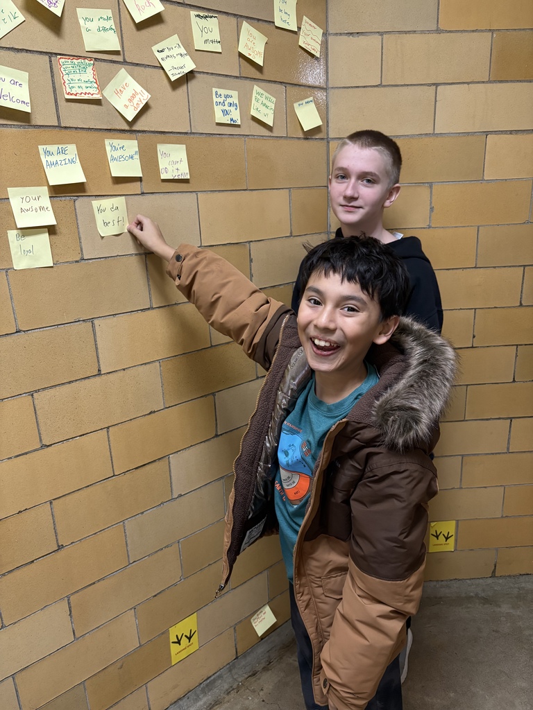 Students pointing to post it with positive note on the wall. 