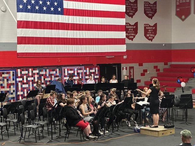 Photo of a band performance with large American flag overhead.
