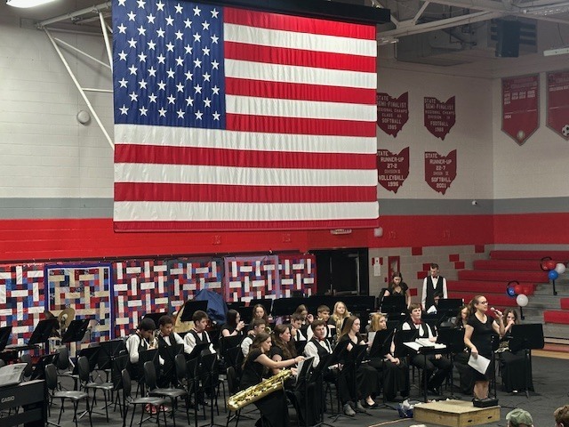 Photo of a band performance with large American flag overhead.