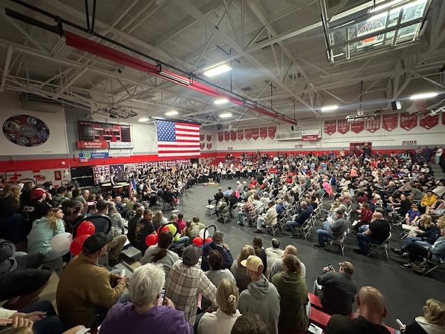Photo of a band performance with large American flag overhead.