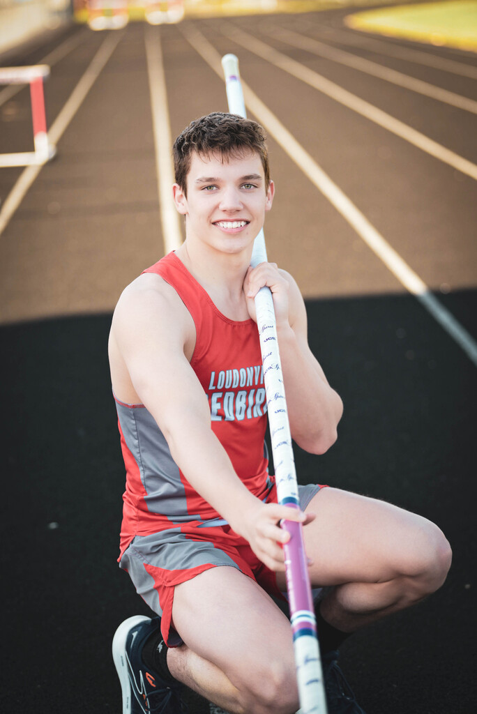 Photo of Cooper holding pole for pole vault in track uniform.