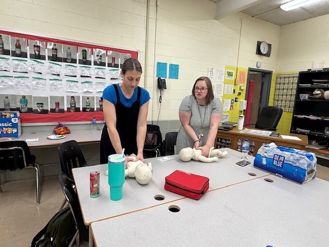 Staff members practicing CPR on baby dummy. 