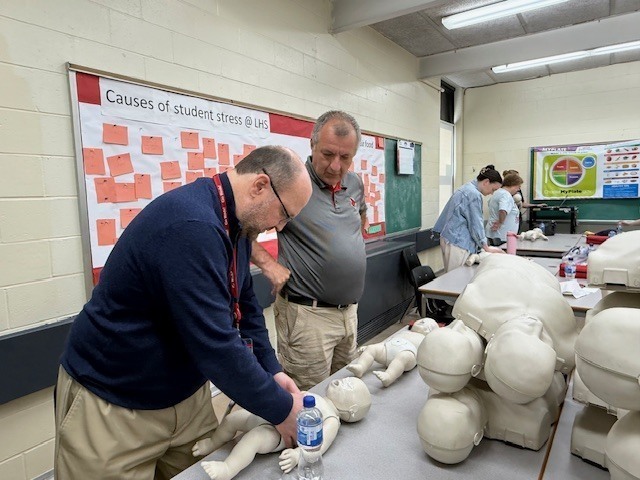 Staff members practicing CPR on baby dummy. 