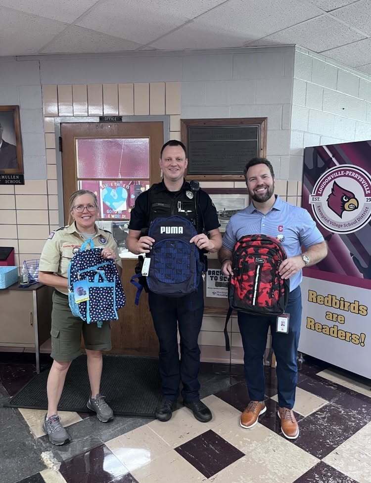 Scouting America representative with Officer Kick and Principal Brumfield holding donated backpacks.
