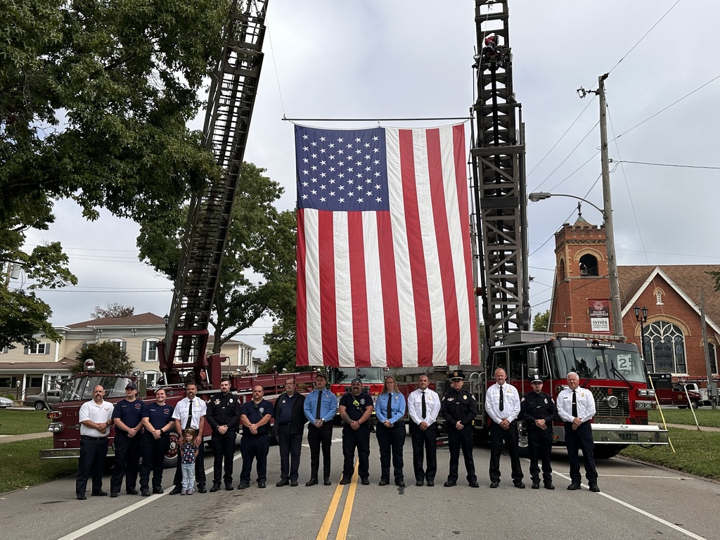 Line of first responders in front of fire truck flying the American flag. 