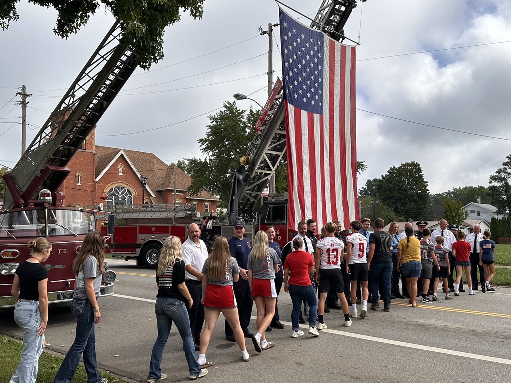 Line of students thanking first responders in front of fire truck flying the American flag. 