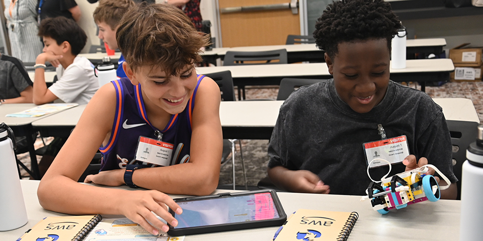 Two students smiling working on a project in a classroom.