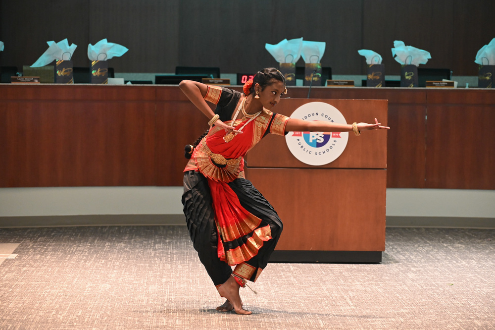 Person performs a traditional cultural dance in a red and black costume inside the LCPS board room.