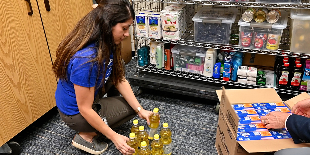 Woman organizing multiple bottles of cooking oil on the floor in a kitchen pantry area.