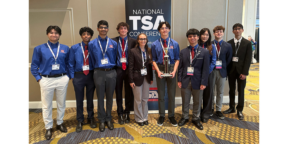 Group of young professionals in blue shirts and suits posing with a trophy at the National TSA Conference.
