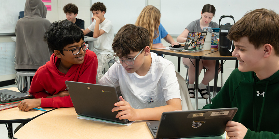 Students gathered around a table with laptops