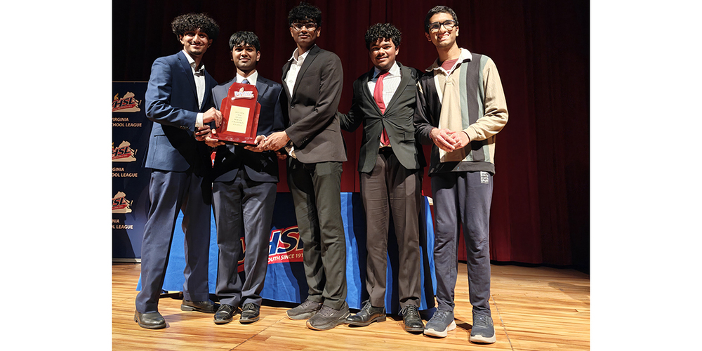 Five young men stand on a stage with a red curtain backdrop, holding a plaque award together in formal and semi-formal attire.