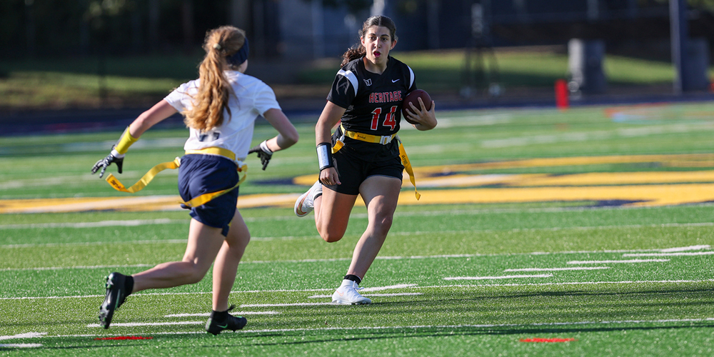 Two girls playing flag football outside on a football field.