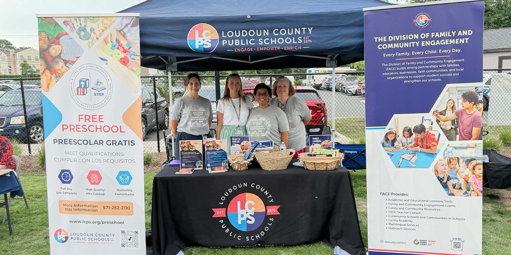 Four representatives stand behind a Loudoun County Public Schools booth promoting free preschool and family engagement programs at an outdoor event.
