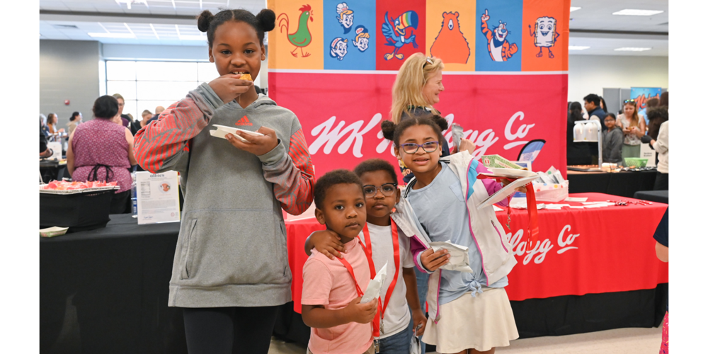 Group of kids sampling food at a Kellogg's booth decorated with vibrant mascot illustrations during a public event.