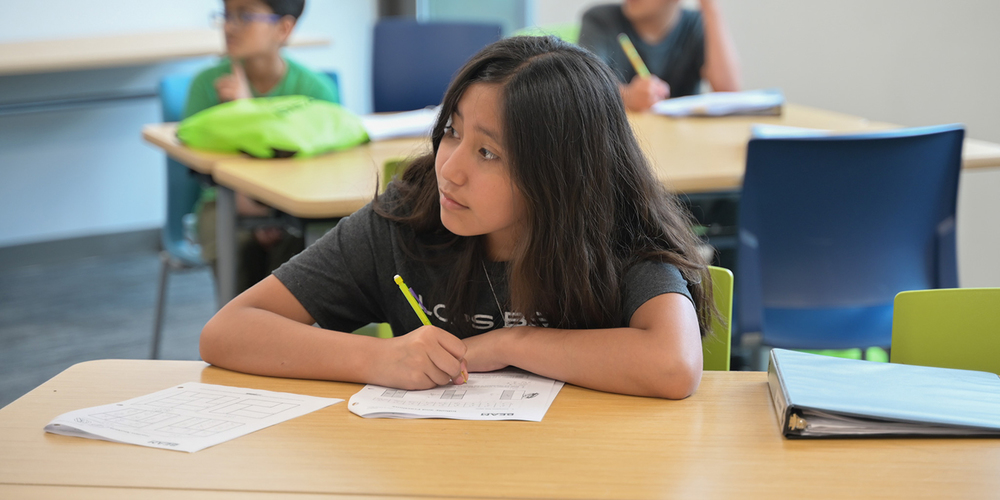 Student focused on writing answers during a classroom test with papers and pencil in hand.