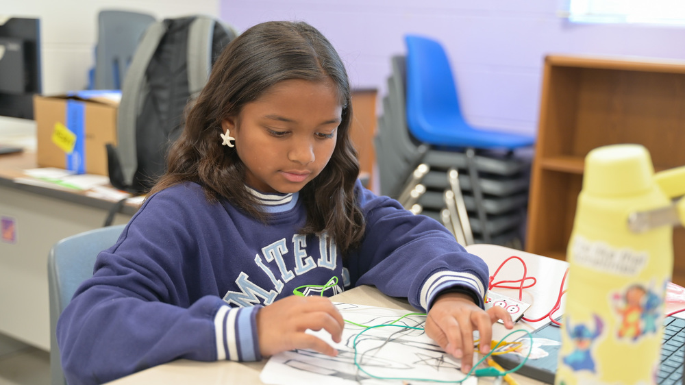 Girl working on a project with wires at a school table.