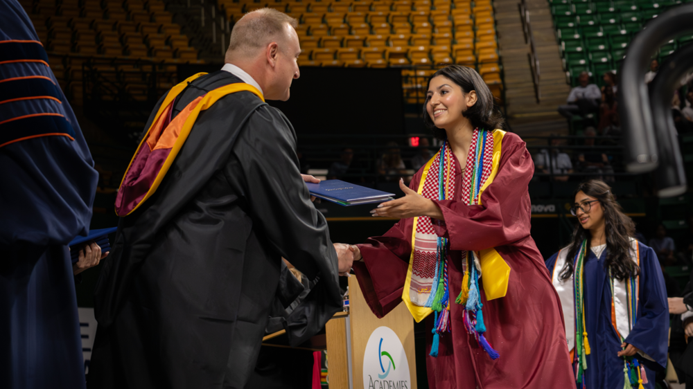 Graduate in a cap and gown smiles while shaking hands and receiving a diploma during a LCPS graduation ceremony.