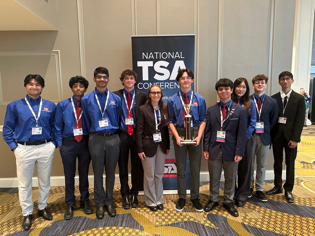 Group of young professionals in blue shirts and suits posing with a trophy at the National TSA Conference.