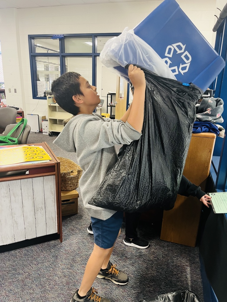 Student in a school front office dumping recyclables from a blue bin with a recycle logo into a bag.