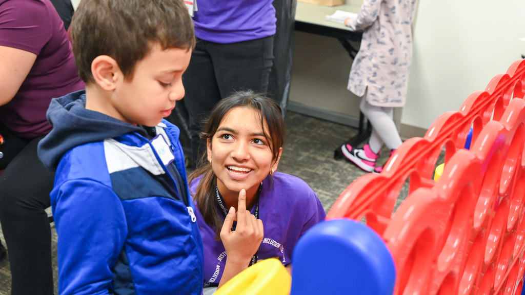 Child in blue jacket playing a game with a woman in purple shirt at a table indoors.