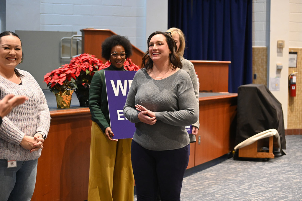 Group of women standing indoors near a wooden podium with poinsettia plants in the background during an event.